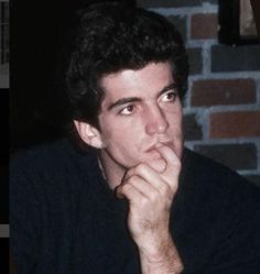 a man sitting in front of a brick wall with his hand on his chin looking to the side