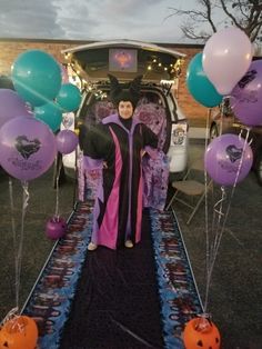 a woman standing in front of a car with balloons and decorations on the ground next to it