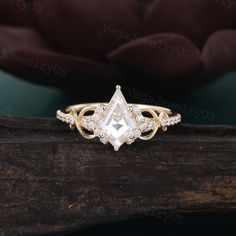 an engagement ring with a pear shaped cut diamond surrounded by smaller round diamonds on a piece of wood