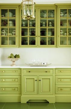 a kitchen filled with lots of green cupboards and white counter top space under a chandelier