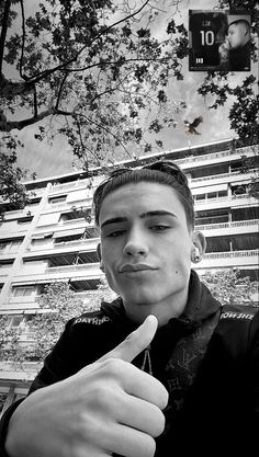 black and white photograph of a young man giving the thumbs up sign in front of an apartment building