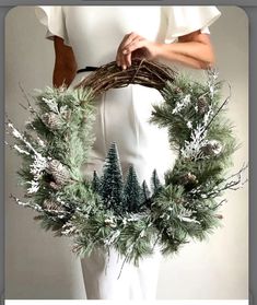 a woman holding a wreath with pine cones and evergreens