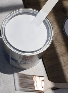 a paint can with a brush in it next to a wooden floor and a painting roller