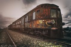 an old rusted train car sitting on the tracks under a cloudy sky with dark clouds