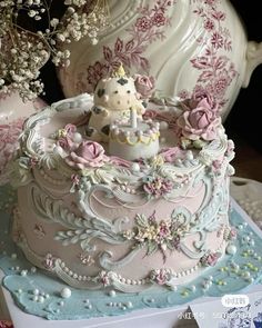 there is a cake decorated with flowers and a unicorn on the top, sitting in front of a teapot