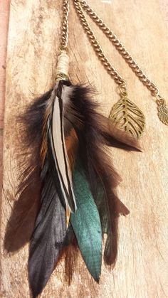 a necklace with feathers hanging from it on a wooden table next to a gold chain