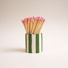 a green and white striped cup with pink tipped matchesticks sticking out of it