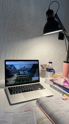 an open laptop computer sitting on top of a desk next to a lamp and books