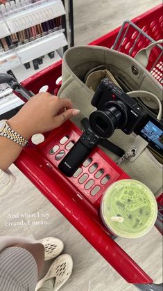 a person holding a camera in front of a shopping cart with other items on it