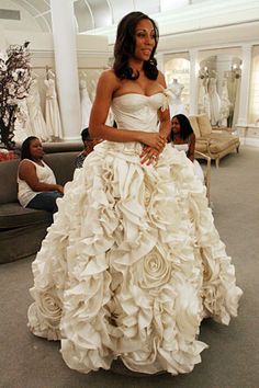 a woman in a wedding dress standing in a room with people sitting on couches