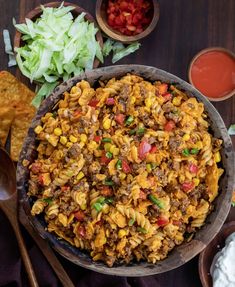 a wooden bowl filled with pasta and vegetables next to other bowls of dips, sour cream and tortilla chips