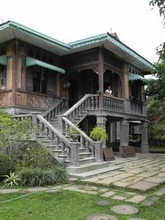 an old wooden house with stairs leading up to the second floor and two people sitting on the balcony