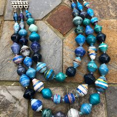 a necklace made out of glass beads on a stone floor next to a pair of earrings