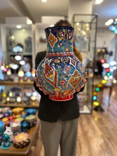 a woman is holding a vase in her hands and looking at the glass case behind her