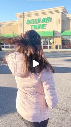 a woman is walking down the street in front of a dollar tree store with her hair blowing in the wind