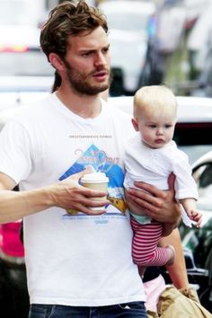 a man holding a baby in his arms while walking down the street with other people