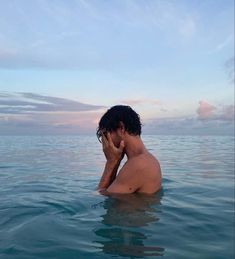 a man sitting in the water on his cell phone looking out at the ocean while holding his head to his ear