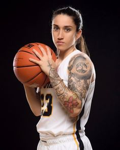 a woman with tattoos holding a basketball in her right hand and looking at the camera