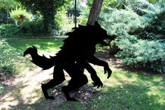 a silhouette of a creature is shown in the grass near trees and bushes, with one arm extended to the ground