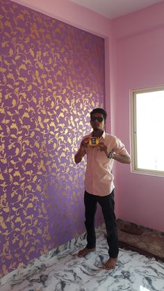 a man standing in front of a purple wall with gold leaf designs on it, taking a selfie