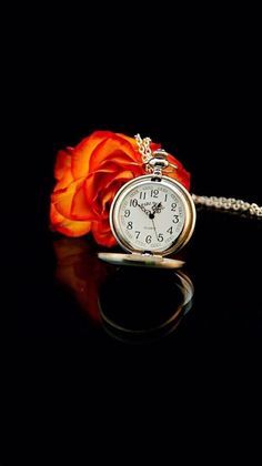 an orange rose sitting on top of a table next to a small pocket watch necklace