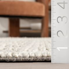 a ruler that is measuring the height of a rug on a wooden floor with a chair in the background