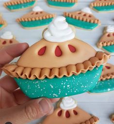 a hand holding a pastry shaped cookie with icing on it's top and other cookies in the background