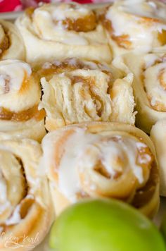 cinnamon rolls with icing sitting on top of a plate next to green apple slices