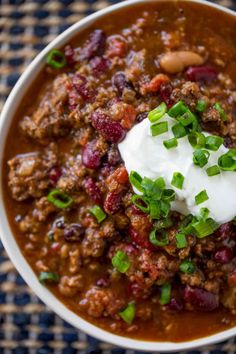 a white bowl filled with chili and sour cream on top of a blue table cloth