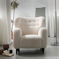 a white chair sitting in front of a window next to a lamp and a book