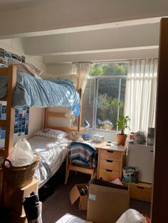 a bedroom with two bunk beds and boxes on the floor in front of it, next to a window