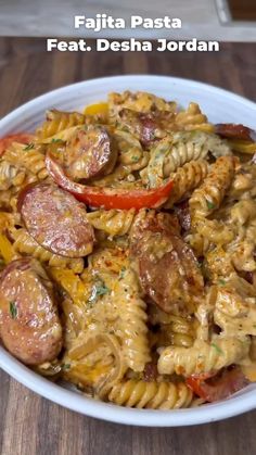 pasta with sausage and peppers in a white bowl on top of a wooden table next to a fork