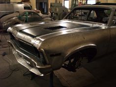 an old car is being worked on in a garage with other cars and machinery behind it