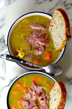 two bowls of soup with ham, carrots and bread on a marble counter top