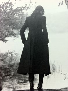 a woman in a long coat is standing by the water