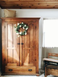 a wooden armoire sitting next to a window with a wreath on top of it