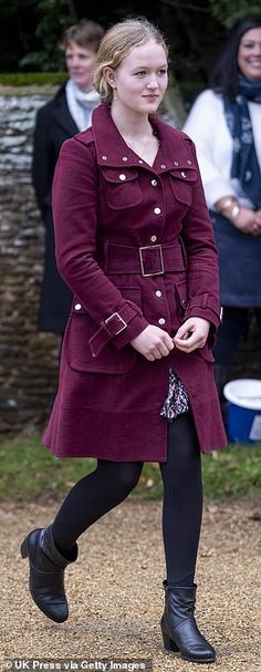 a woman in a red coat and black boots is walking with other people behind her