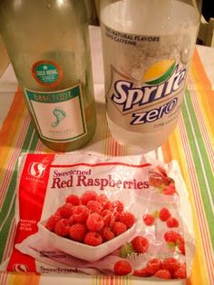 raspberries and water on a table next to a bag of chips, bottle of soda