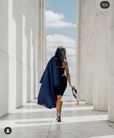 a woman in a black dress is walking down the street with a blue coat over her shoulders