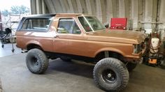 an old ford bronco is parked in a garage with large tires on the front