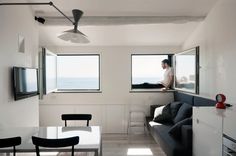 a person sitting on a couch in a room with two windows and a television mounted to the wall