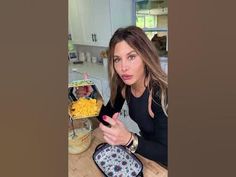 a woman sitting at a kitchen counter pointing to the camera