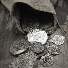 a pile of coins sitting on top of a wooden table next to a cloth bag