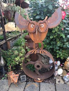 an owl statue sitting on top of a metal object in the middle of a garden