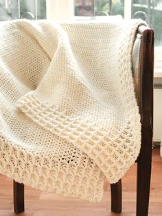 a white knitted blanket sitting on top of a wooden chair next to a window