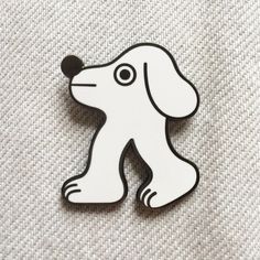 a white and black dog brooch sitting on top of a gray fabric covered floor