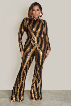 a woman standing in front of a wall wearing a gold and black sequin jumpsuit