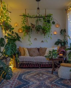 a living room filled with lots of plants next to a wall covered in hanging lights