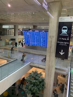 people are walking through an airport terminal with signs on the wall and stairs leading up to them