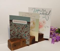 some cards are sitting on wooden blocks with flowers in the background and greeting cards attached to them